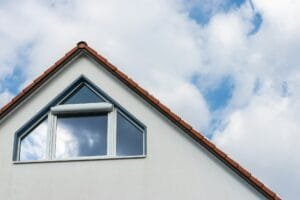 A fragment of the roof and attic floor of a white private house against a blue sky with clouds